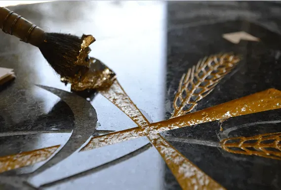 Application minutieuse de feuilles d'or au pinceau sur une gravure en pierre.